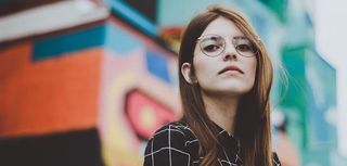 woman in plaid shirt with glasses standing in front of colorfully painted building