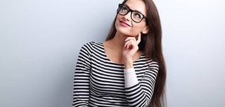 Pretty casual thinking woman in glasses looking up on blue background with empty copy space