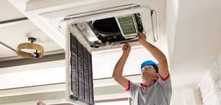 man on ladder installing air conditioning unit in ceiling opening