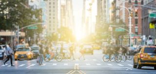 People crossing the busy intersection between traffic on 3rd Avenue and 10th Street in Manhattan in New York City with the glow of sun light in the background