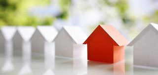 row of several small wooden house models all are white but one blurred trees in background