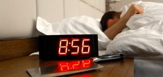 alarm clock reading four minutes to nine in foreground and person sleeping in bed in background