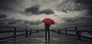 A woman holds a red umbrella on a fishing pier during a storm.