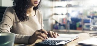 Portrait of a concentrated Asian accountant at her workplace using her calculator. Concept of accounting in business.