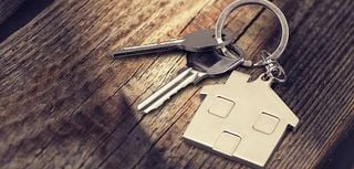 keys on a keychain shaped like a house laying on a piece of wood