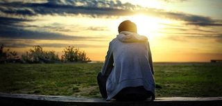 Man sit on the Bench looking out a sunset over grassy field