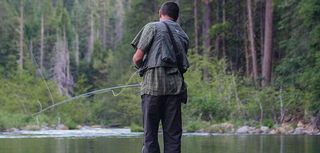 fisherman standing on log near lake casting fishing pole in forest setting