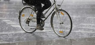 closeup of lower half of a person riding a bicycle in heavy rain on city street