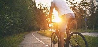 The young guy in casual clothes is cycling on the road in the evening city