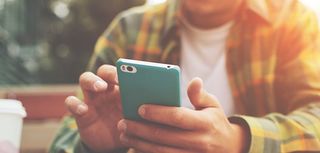 Young man with smartphone in hand sitting in cafe, texting