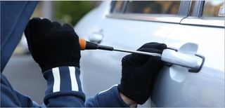 thief breaking into a car using screwdriver to unlock door