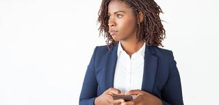 Serious pensive office employee using smartphone, texting message, looking away. Young African American business woman standing isolated over white background. Communication concept